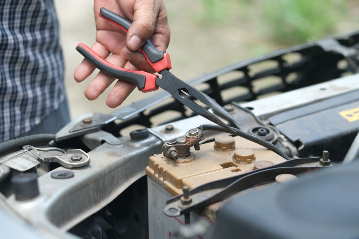 A hand holding a red and black battery clamp