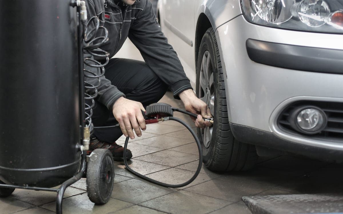A person crouched at a car wheel inflating a tire